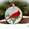 A handmade wood slice Christmas ornament with a hand-painted red cardinal against a gray winter background at Cove Creek Photography.